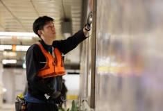 地下鉄の駅で男性作業員が壁面広告の作業をしている